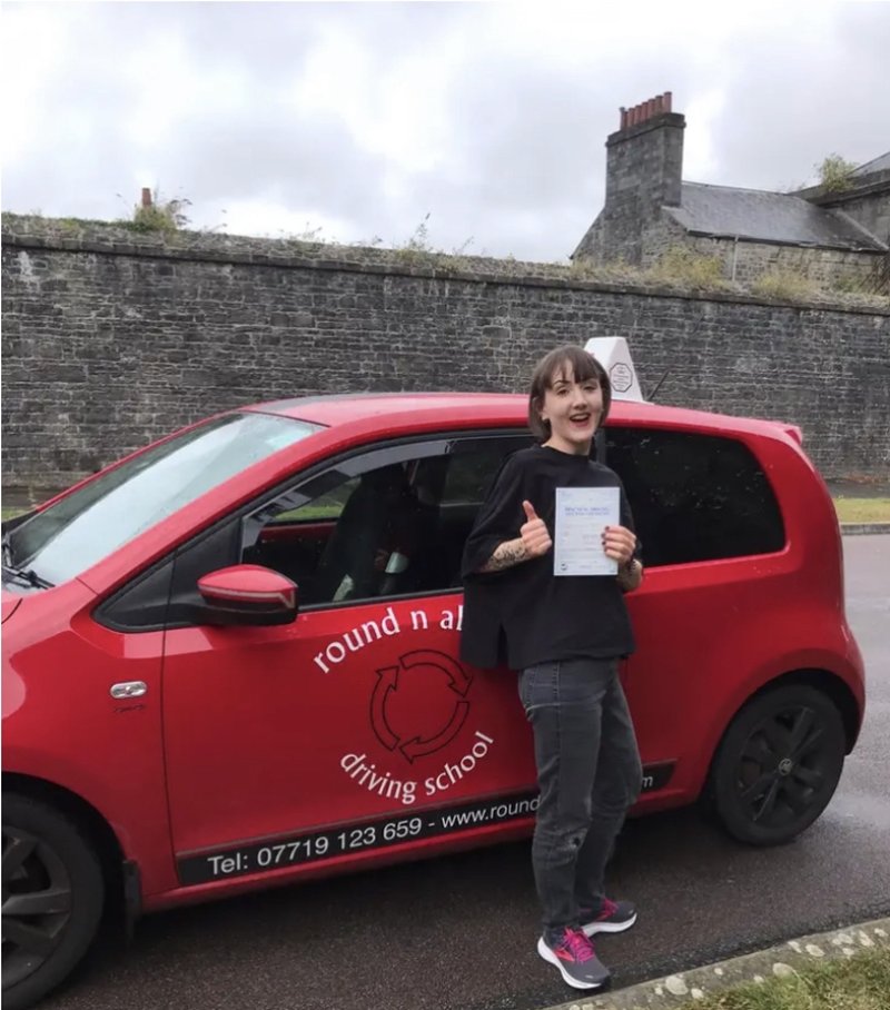 Leanne holding her driving test pass certificate next to a red car